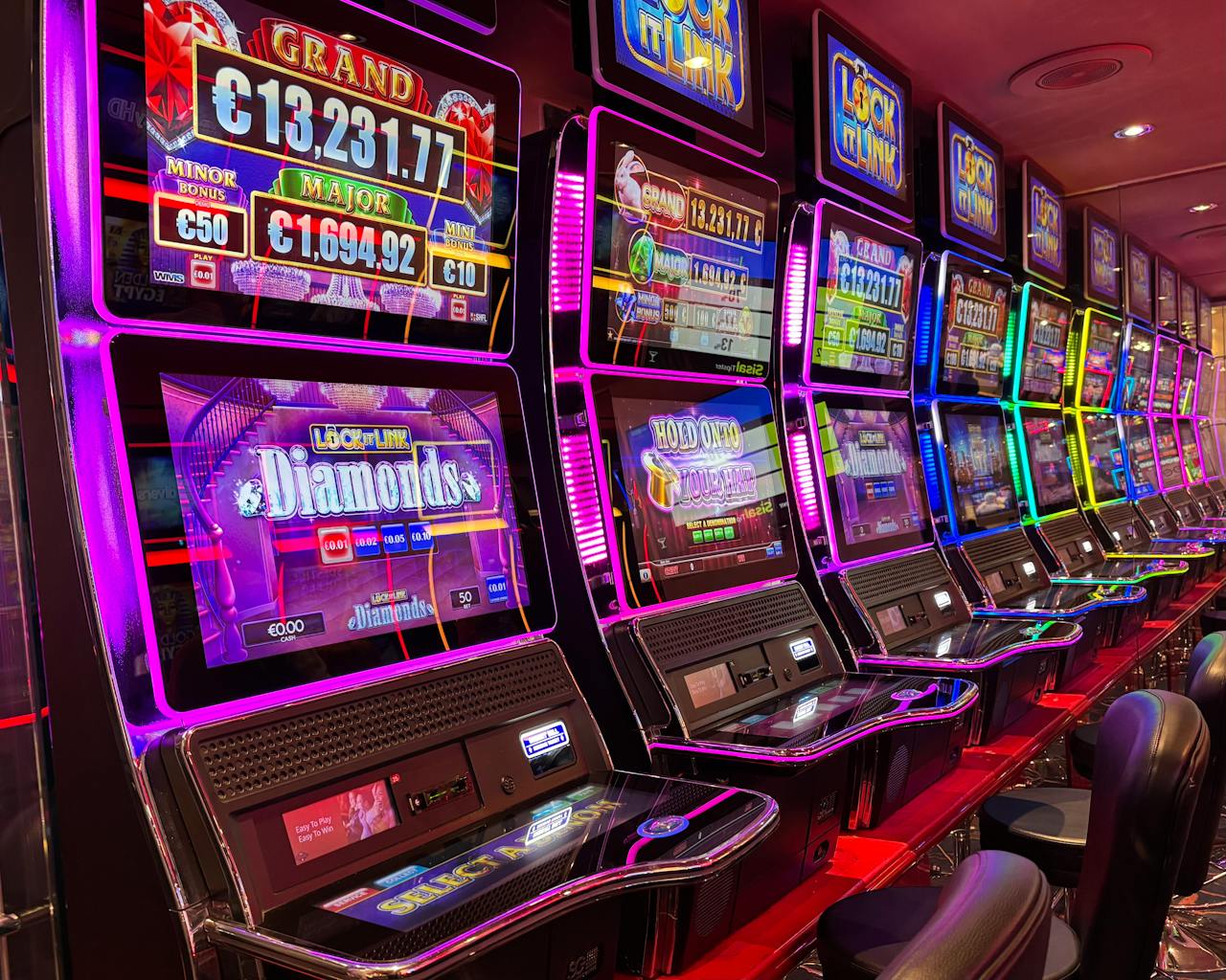 Colorful slot machines lined up in a casino with neon lights and jackpot displays.